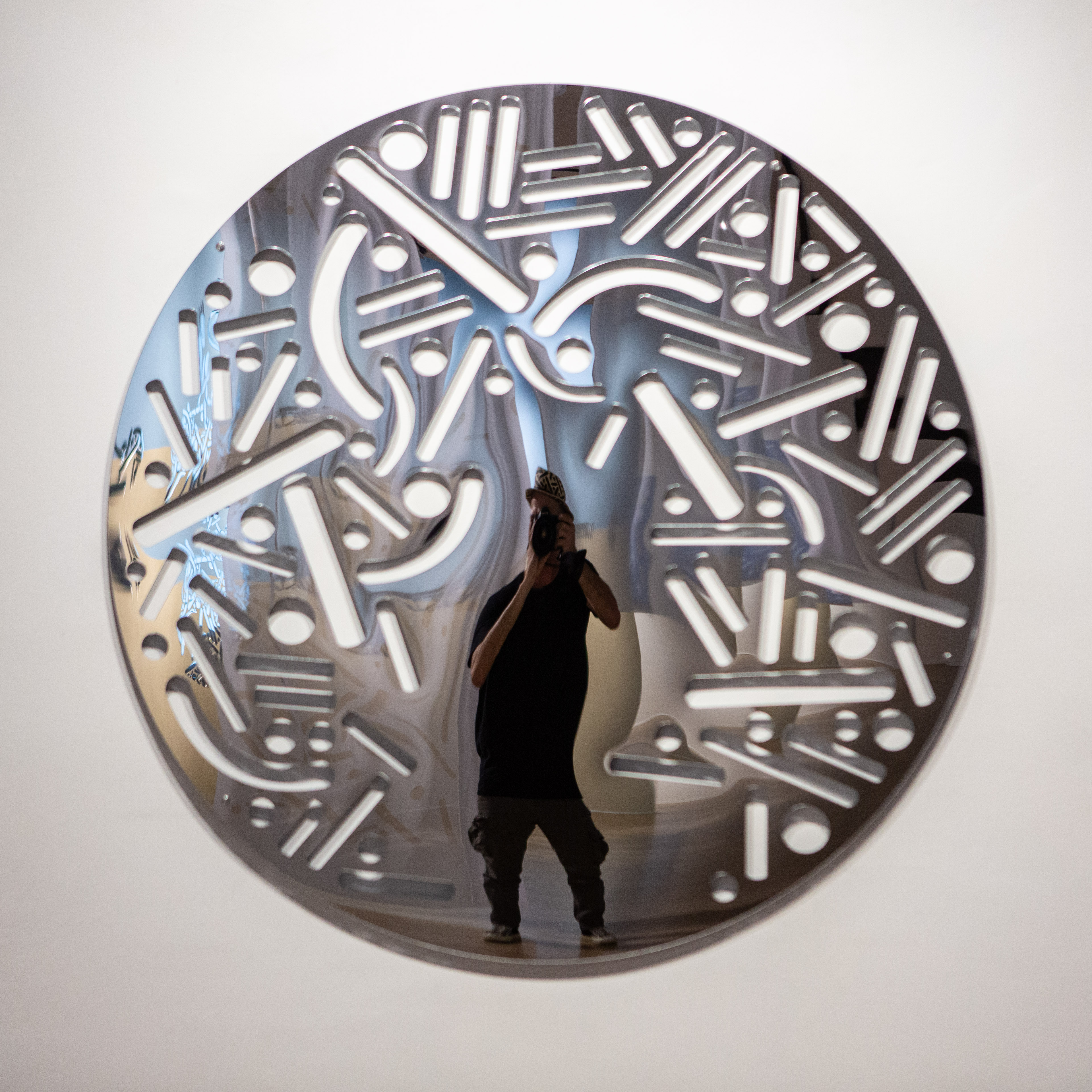 Person stands before a large reflective circular artwork filled with luminous dots and lines.