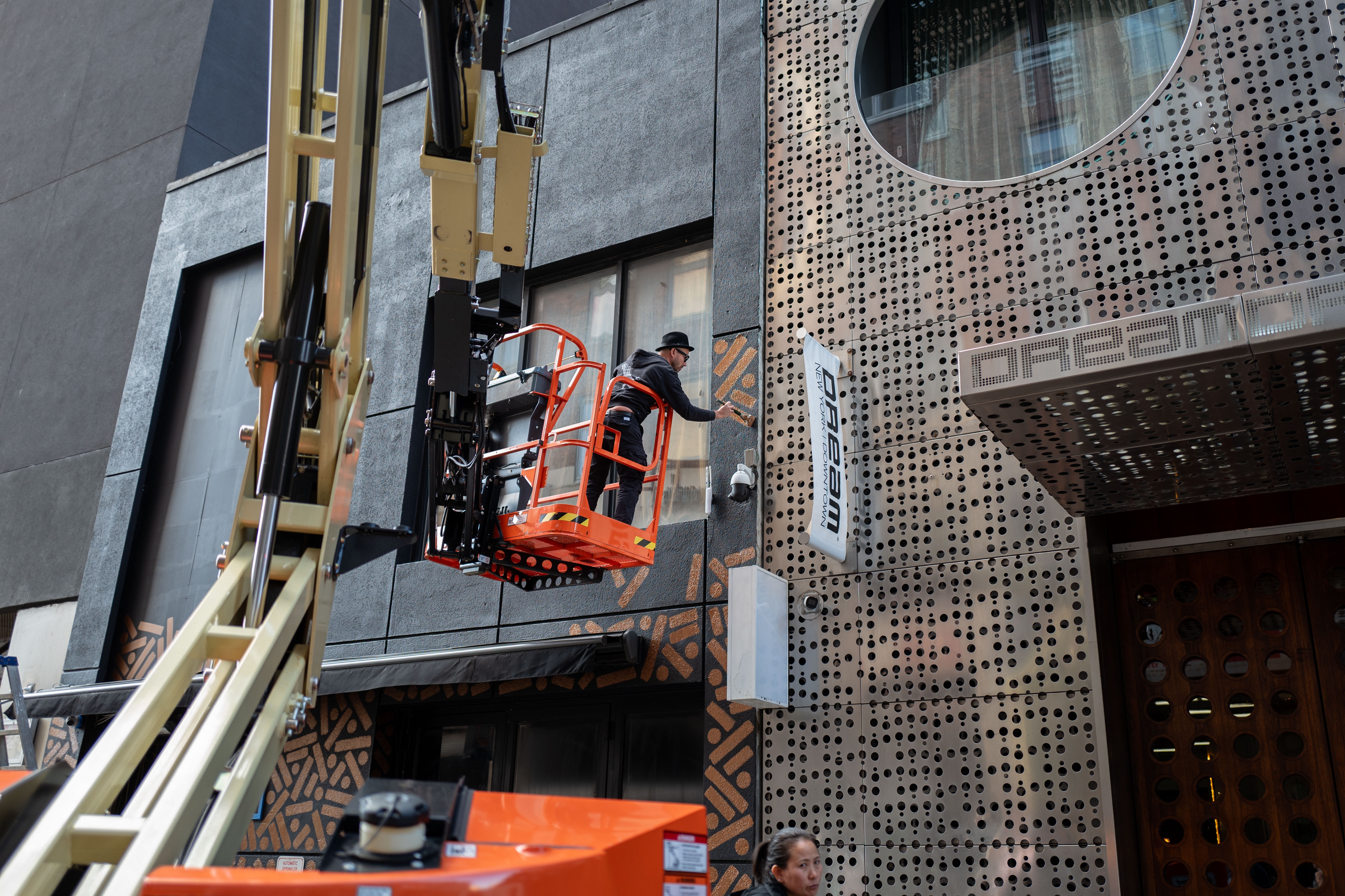 The Golden Weave: Artist works from a raised lift to paint a large patterned storefront facade.