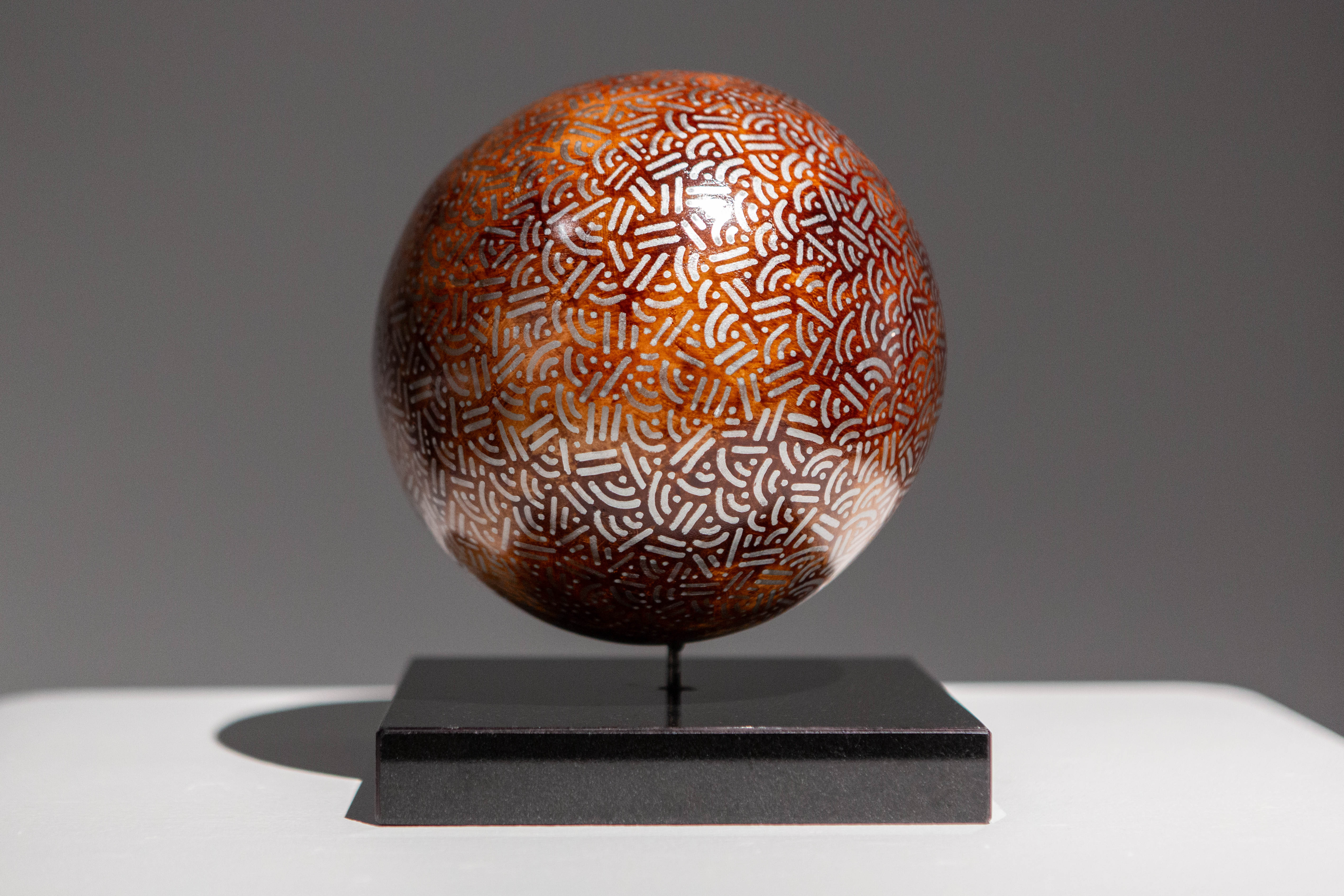 Copper-colored sphere covered in dots and lines displayed on a black pedestal.