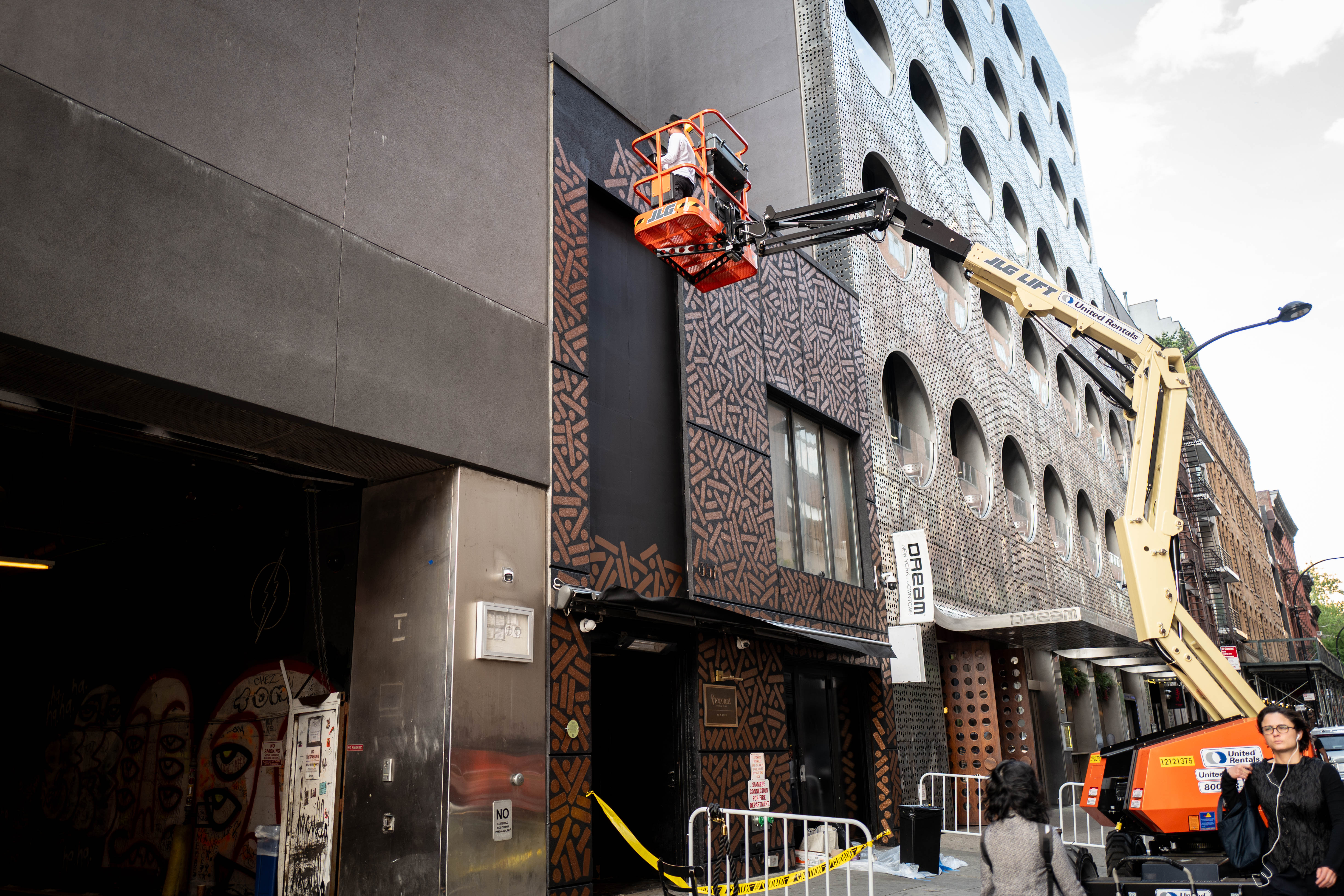 The Golden Weave: Artist works from a raised lift to paint a large patterned storefront facade.