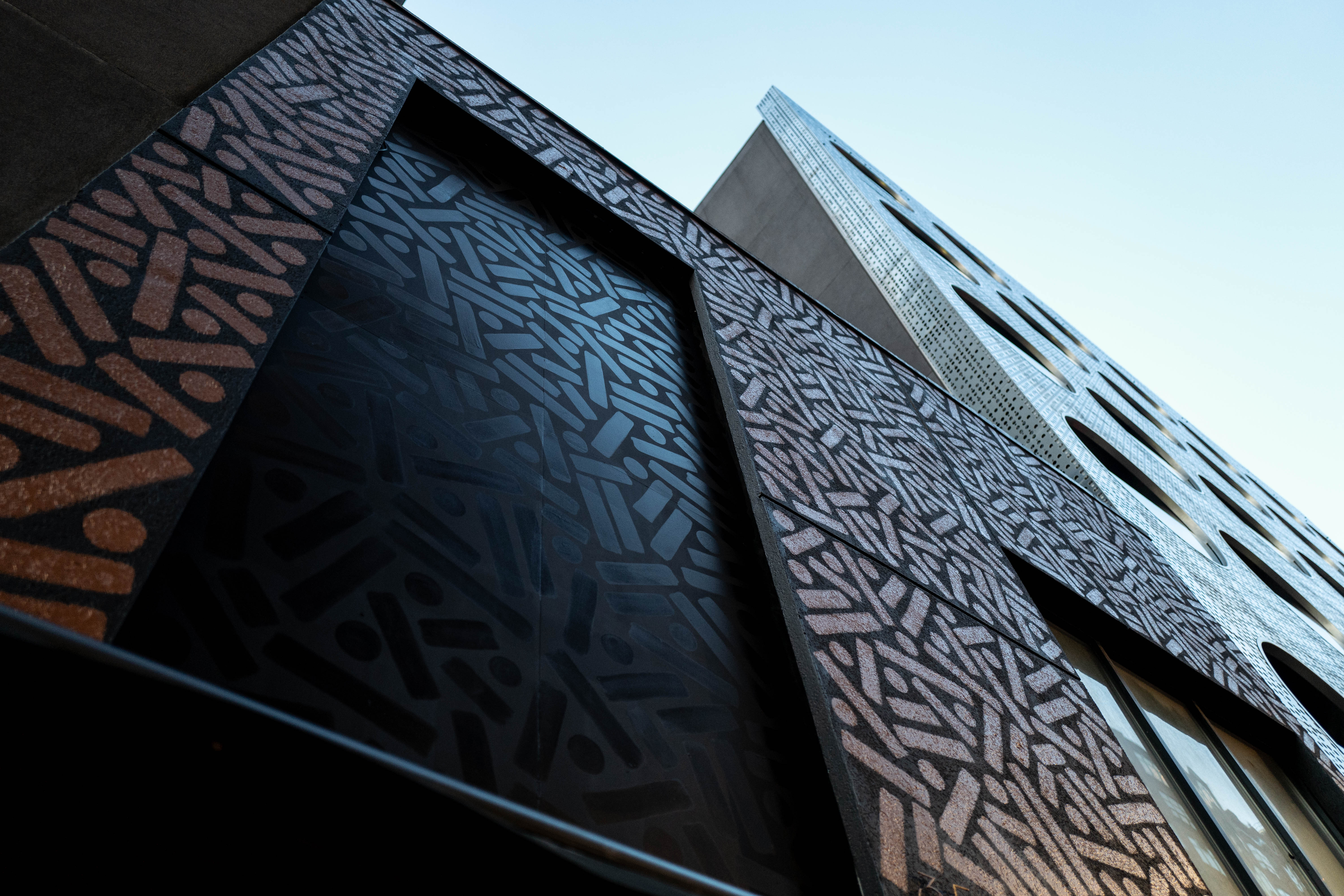 The Golden Weave: Upward view of golden dots and lines covering a tall dark building facade.