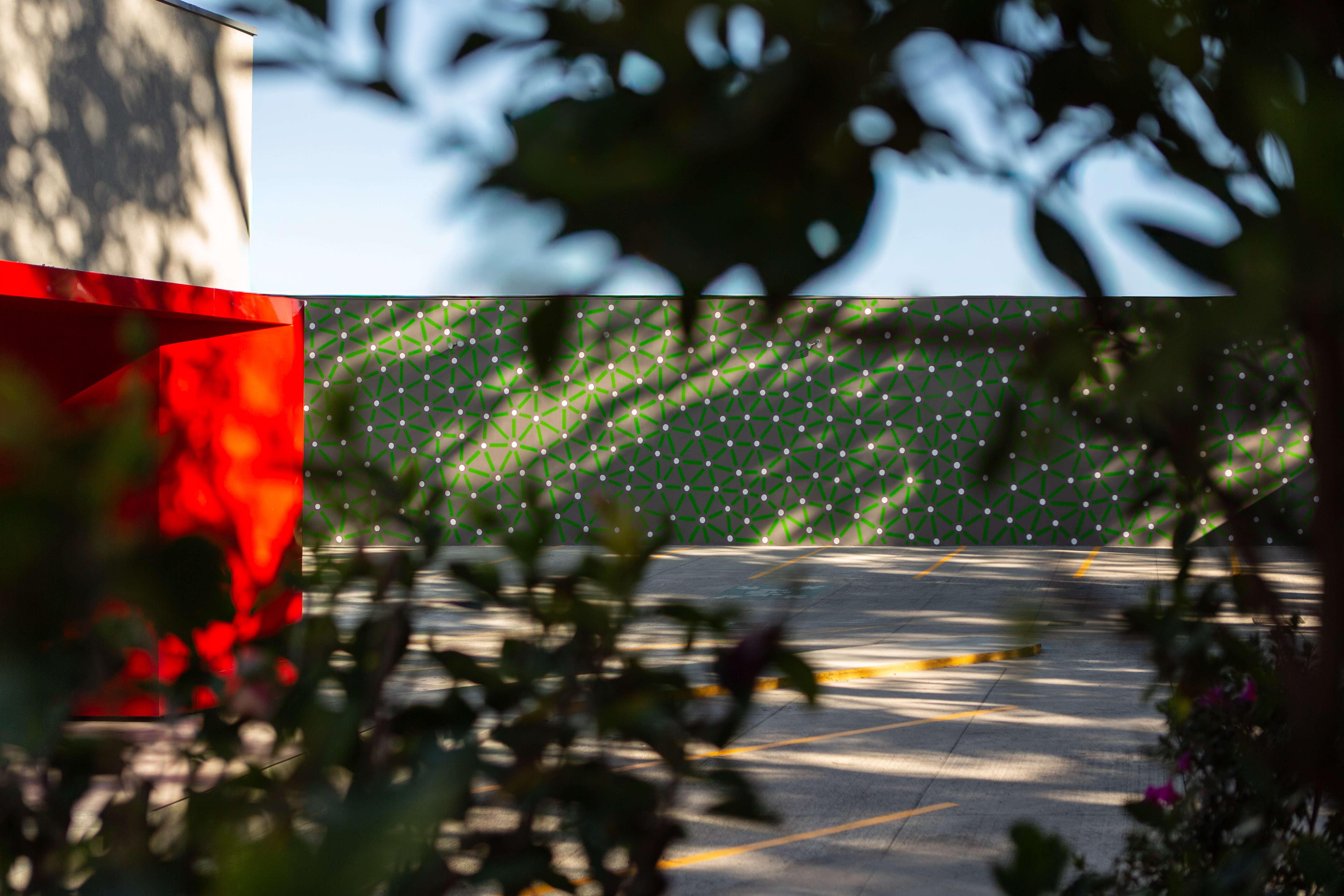 Sunlight and foliage cast shadows across green and red mural surfaces in a garden.
