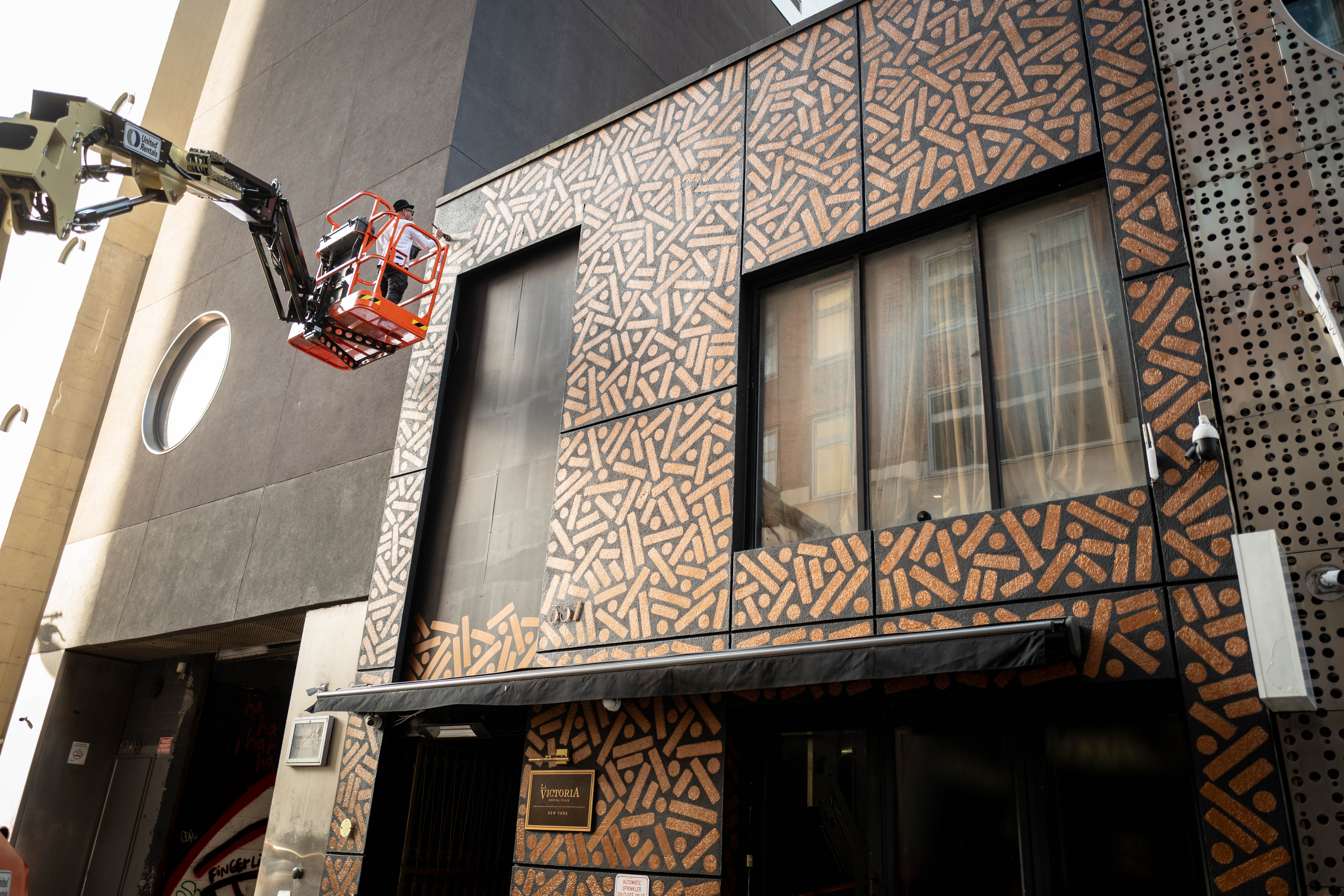 The Golden Weave: Artist works from a raised lift to paint a large patterned storefront facade.