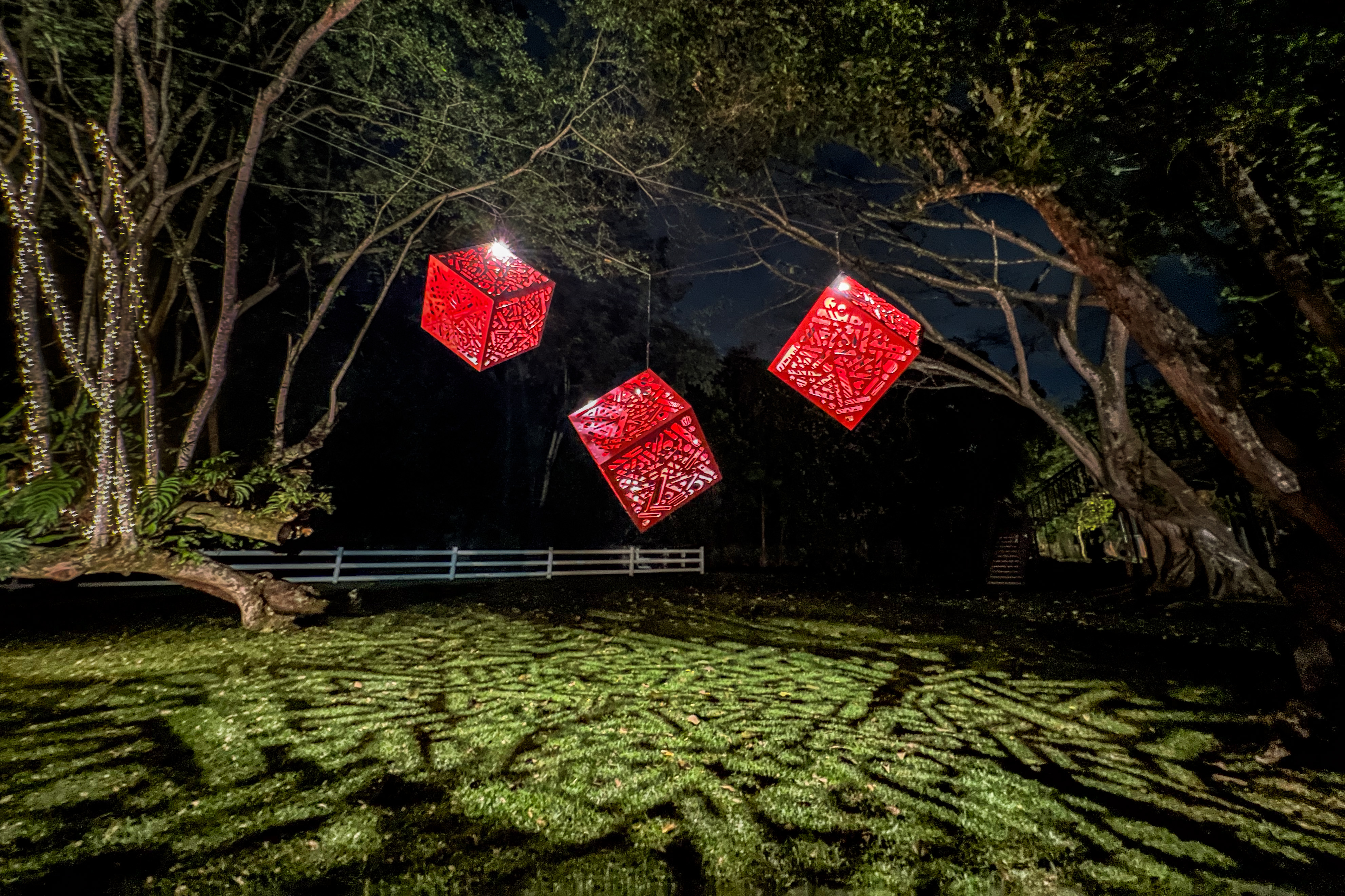 Hemoglobin: Three illuminated red cube sculptures at night, casting patterned shadows onto the ground.