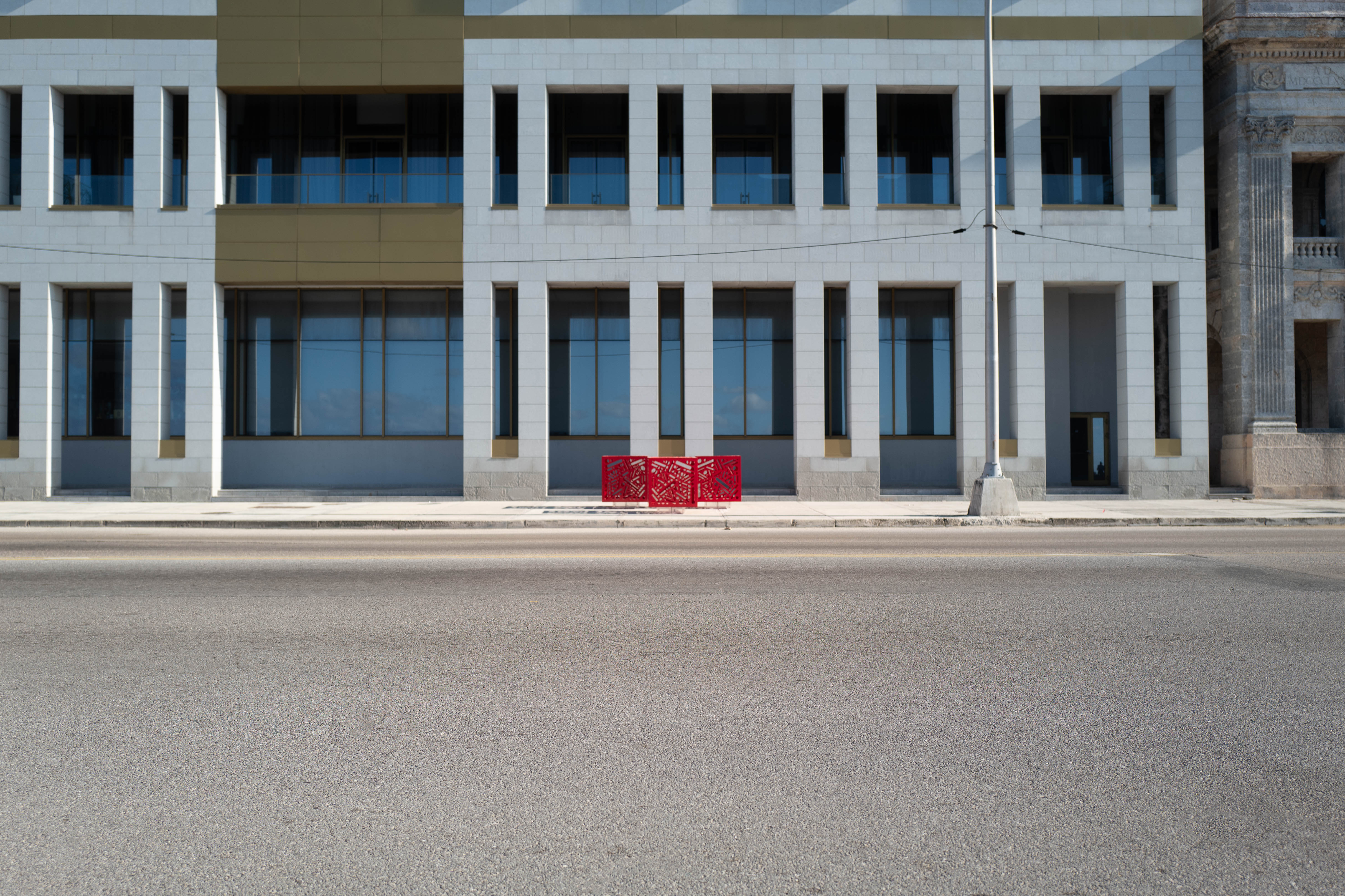 Hemoglobin - Installation of 3: Three red cutout cube sculptures on a city sidewalk beside a road and a large building.