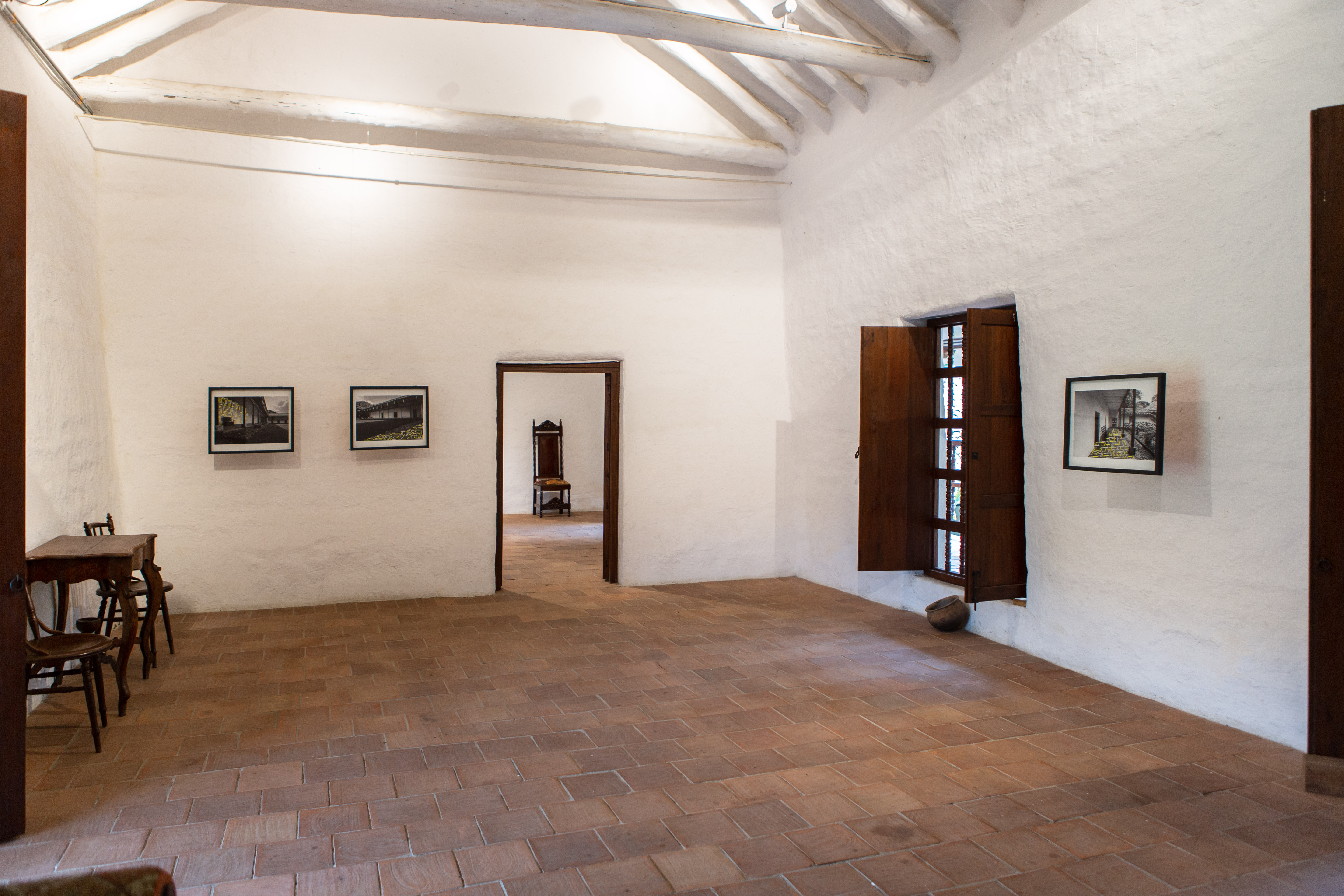 Exhibition view of Pipe Yanguas’s photographic works displayed inside the historic Hacienda Cañasgordas in Cali, Colombia, featuring white walls, wooden architectural details, and terracotta floors.