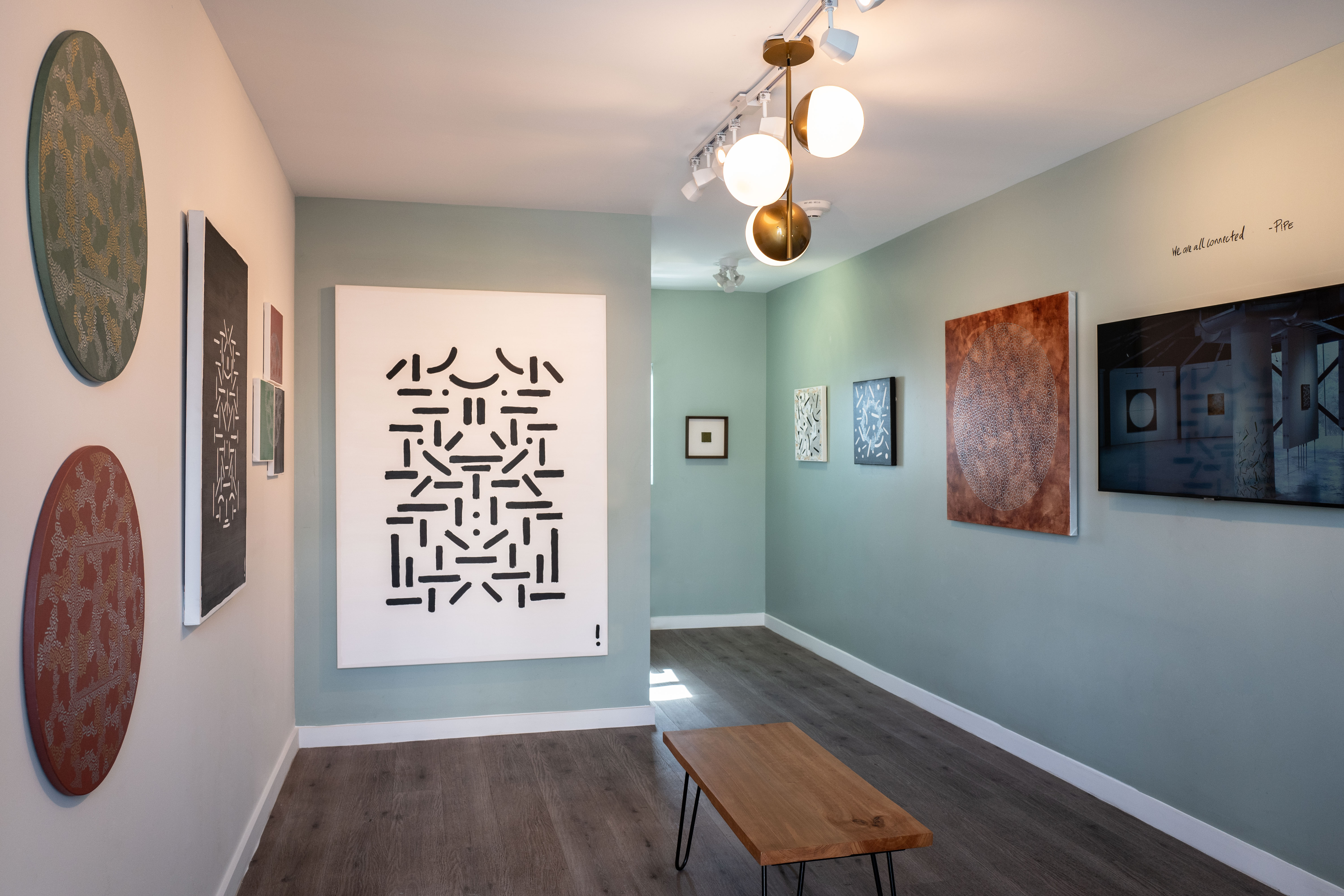 Installation view of Pipe Yanguas’s artwork at Feria Clandestina during Miami Art Week 2024, featuring a large black-and-white geometric composition displayed in a gallery with pale green walls, wooden floors, and works by other artists.